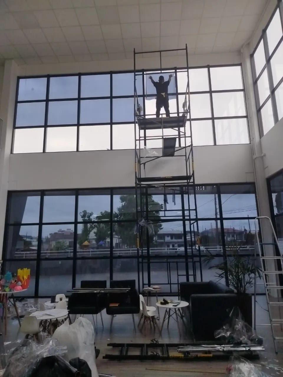 Instalador em andaime aplicando película em janela alta