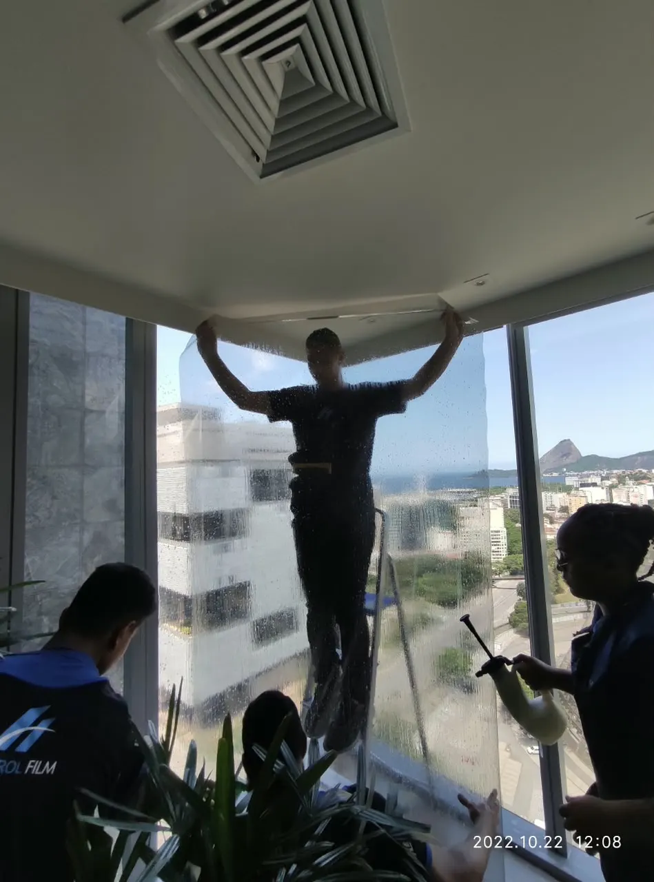 Instalador aplicando película em janela de canto de escritório