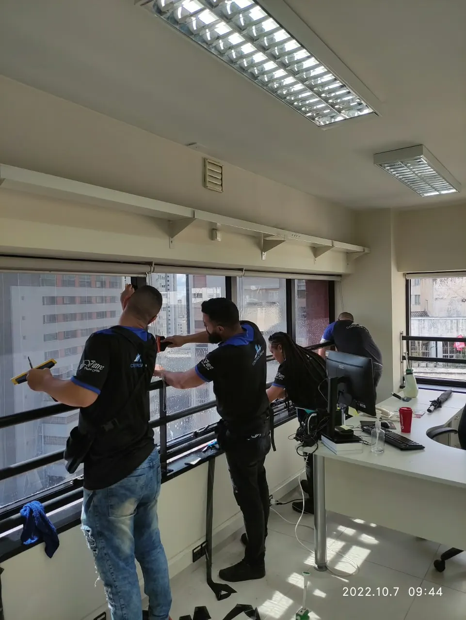 Equipe aplicando película nas janelas de uma sala comercial